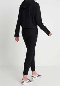 Zwarte kort gesneden hoodie met capuchon, gecombineerd met zwarte strakke legging en zwart-witte slip-on schoenen met dambordpatroon. Simpel ontwerp en textuur.