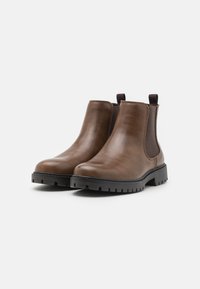 Botas Chelsea de cuero marrón con paneles laterales elásticos, punteras redondeadas y suelas de goma negra resistente; cuentan con lengüetas en la parte posterior para facilitar su uso.