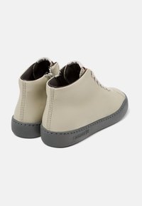 Botas de tobillo de cuero beige con suelas de goma gris, que cuentan con una textura suave, cordones en la parte delantera y detalles de costura a lo largo de los bordes.