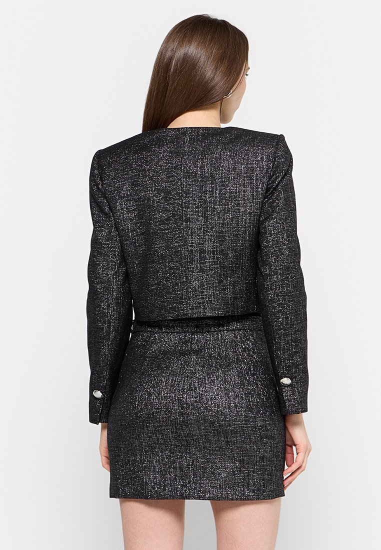 Blazer noir tissé au design ajusté, avec une coupe cropped, des accents de boutons en argent et une mini jupe assortie, mettant en avant une finition texturée.