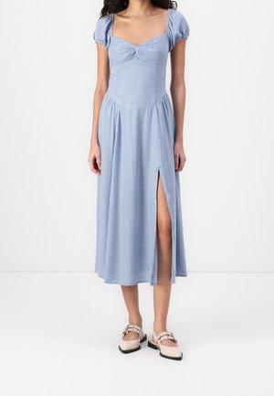 Robe midi en vichy bleu avec des manches bouffantes et un col carré. Présente une fente latérale et un corsage ajusté, fabriquée en tissu léger.