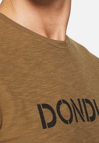 Olivengrøn t-shirt med rund halsudskæring og sort tekst, der står "DOND" i fed skrift, fremstillet af et struktureret stof.