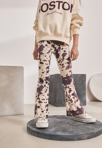 Knit, beige flared pants with maroon splatter pattern. Paired with a cream sweatshirt featuring "BOSTON" logo and white sneakers.