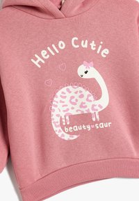 Różowa bluza z kapturem z białym graficznym wzorem dinozaura w różowe kropki, tekstem "Cześć, Słodziaku" i "uroda-saur", oraz prążkowanymi mankietami i dołem.