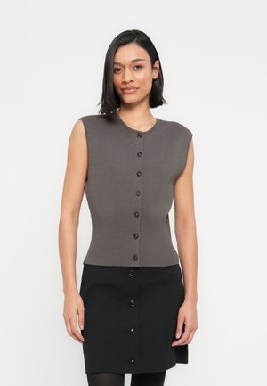 Haut gris sans manches en tricot avec un col rond et des boutons noirs sur le devant, associé à une jupe noire avec des détails à boutons.