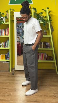 Gray, relaxed-fit trousers with side pockets, paired with white sneakers. The backdrop features yellow walls and green shelves with books.