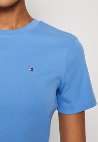 Lyseblå bomull T-skjorte med ribbestruktur, med en liten brodert logo i rød, hvit og blå på brystet. Klassisk rund hals-design.