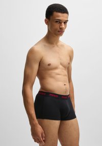 Bóxers negros con un ajuste ceñido, con una amplia cintura elástica que lleva el nombre de la marca "HUGO" en rojo. Textura suave y diseño minimalista.