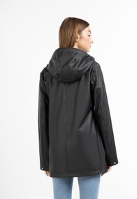 Jachetă impermeabilă neagră cu glugă, cu o textură netedă și lucioasă și o croială lejeră. Vedere din spate care arată un design simplu și hardware minimal.
