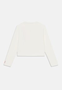 Przycięty biały longsleeve wykonany z gładkiego materiału. Posiada okrągły dekolt i mały detal z logo na rękawie.