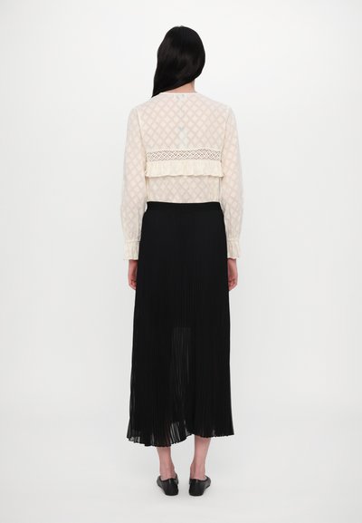 Blusa blanca de manga larga con una textura estampada y con un borde de encaje, combinada con una falda midi plisada negra.