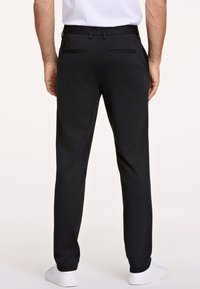 Schwarze Hosen mit maßgeschneiderter Passform, Gesäßtaschen und glatter Textur. Kombiniert mit weißen Turnschuhen, die ein sauberes, modernes Design zeigen.