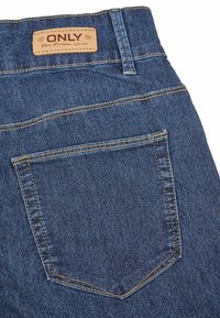 Un jean en denim comportant un tissu bleu foncé avec une texture légèrement usée. Comprend une étiquette en cuir marron et une seule poche arrière avec des détails de couture.