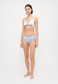 Biely trojuholníkový bralet s čiernym pásom "MOSCHINO I ❤️ YOU", skombinovaný s svetlomodrými bikini nohavičkami s pásom "MOSCHINO". Mäkka textúra látky.