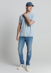 Lichtblauw gestreept T-shirt met korte mouwen, denim jeans en witte sneakers met grijze accenten. Een casual pet maakt de outfit compleet. Eenvoudig ontwerp.