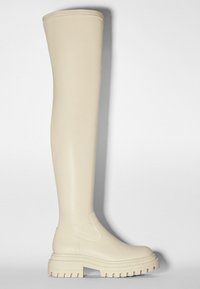 Botas beiges hasta la rodilla, hechas de un material sintético suave, que presentan una suela gruesa con surcos y sin herrajes o patrones visibles.