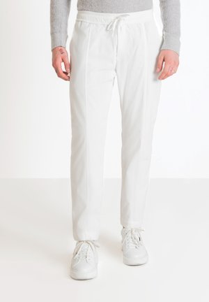 Pantaloni bianchi a costine con vita elasticizzata e cordino. Texture liscia e vestibilità sartoriale, abbinati a sneakers bianche.