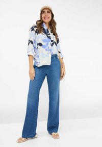 Floral-patterned, lightweight blouse in blue and white, paired with wide-leg blue denim jeans. Accessories include a straw bag and flip-flops.