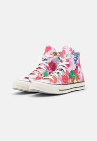 Para wysokich trampek z wielobarwnymi, kwiatowymi wzorami i białymi sznurówkami, gumową podeszwą oraz fakturowanym czubkiem na białym tle.