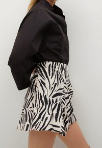 Camicia nera con bottoni abbinata a una gonna beige con stampa a zebre nere, orlo arricciato e silhouette strutturata.