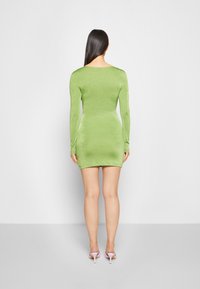Vestido mini de mangas longas e justo, em verde brilhante, feito de um tecido suave e elástico. Apresenta um decote redondo e uma bainha moderadamente curta.