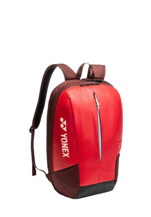 Rode en bruine Yonex-rugzak met gewatteerde riemen, een voorvak met rits en blauwe trekker, en een groot hoofdvak met rits aan de bovenkant.