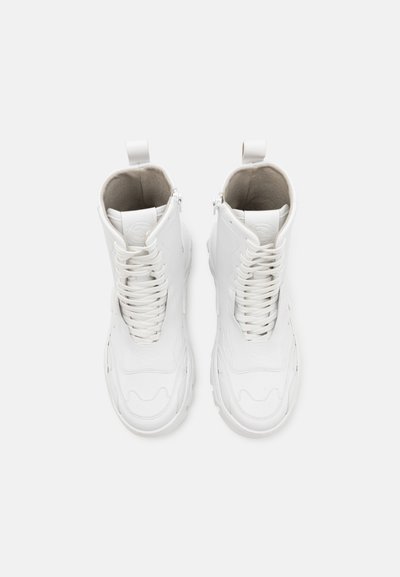 White leather ankle boots featuring a lace-up front, textile lining, circular logo on the tongue, and a sturdy sole.