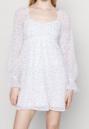 Vit blommig klänning med långa, puffärmar, som har en rynkad midja och lagerkant. Små blå och violetta blommor överallt.
