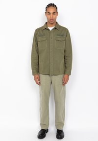 Olive green button-up shirt with two chest pockets, paired with light green cargo pants and black shoes. Smooth fabric with a relaxed fit.