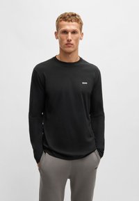 Cămașă neagră cu mâneci lungi, fabricată dintr-un material neted, având un decolteu rotund și un mic logo alb "BOSS" pe pieptul stâng.