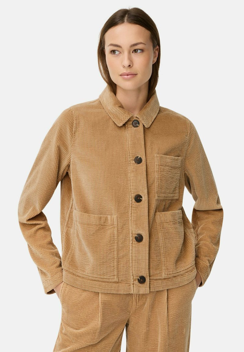 Bruine corduroy jas met een puntkraag, sluiting met knopen aan de voorkant, twee opgestikte zakken en ribbelstructuur. Geschikt voor casual draag.