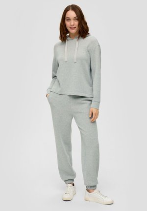 Felpa grigia chiara con cappuccio e corde di regolazione abbinata a pantaloni della tuta con polsini elasticizzati. Sneakers bianche completano l'outfit.