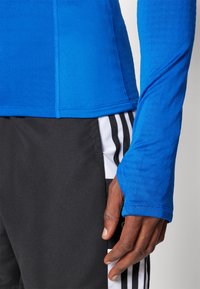 Blå langermet treningstrøye med teksturert overflate og kontrasterende sømdetaljer, kombinert med svarte shorts med hvite striper.