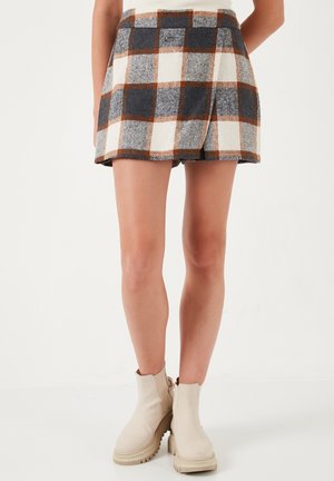 Wollen rok van een bruin, wit en marineblauwe ruitpatroon, met een uitlopende vorm en een elastische taille. Gecombineerd met beige enkellaarsjes.