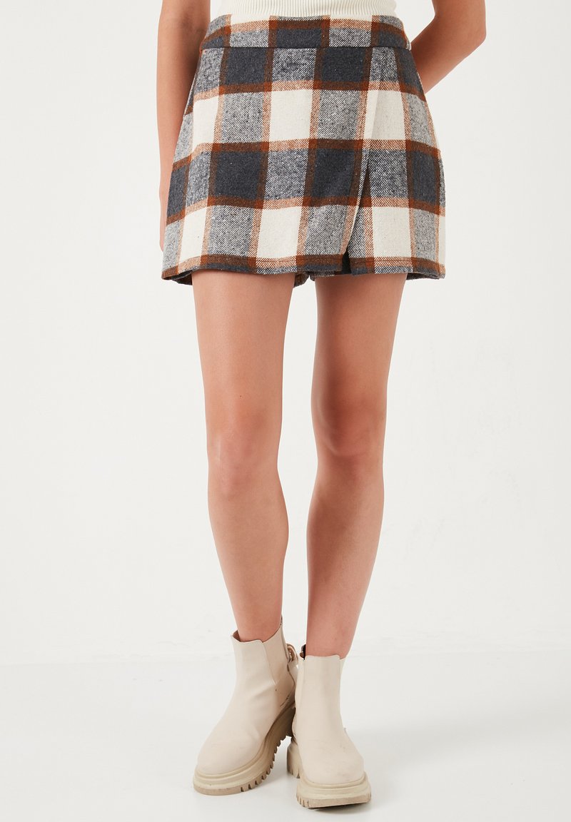 Gonna in misto lana con un motivo plaid marrone, bianco e blu navy, caratterizzata da una forma svasata e vita elastica. Abbinata a stivaletti beige a caviglia.