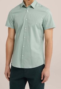 Kortärmad skjorta med knappar i ljusgrön bomull, med krage, framknäppning och rundad nederkant. Bärs med mörkgrön strukturerad byxa.