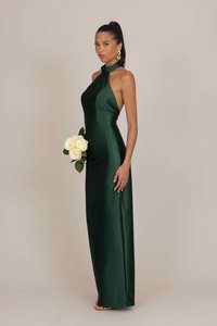 Zelena satenasta obleka z ovratnikom, ki se zavezuje za vrat, s tesnim krojem in stranskim razporkom. Model drži šopek belih vrtnic. Gladka tekstura in eleganten dizajn.