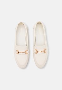 Krémové loaferky vyrobené z hladkého materiálu, s akcentem z řetězu ve zlatém tónu přes přední část. Zaoblená špička a design na obouvání.