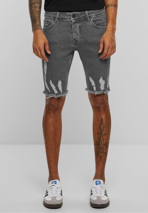 Grå denimshorts med frynset kant og slidte hvide mønstre. Medium talje med traditionelle lommer. Sammen med grå og hvide sneakers.