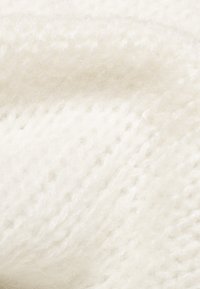 Biała dzianina o miękkiej, teksturowanej powierzchni, prezentująca luźny splot i puszysty wygląd. Idealna na odzież lub akcesoria.