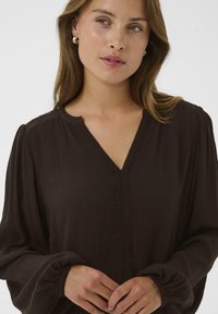 Brun, struktureret blouse med V-hals, blonder og tapered, voluminøse ærmer. Blødt materiale med en afslappet pasform.
