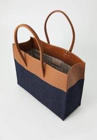 Two-tone tote bag made of navy fabric and tan leather. Features sturdy handles, an open top, and a patterned interior lining.