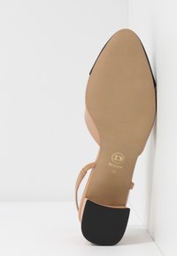 Nude high-heeled sandal with a pointed toe, adjustable strap, and a textured outsole. Features brand logo on the insole and a contrasting heel.