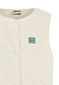 Kamizelka polarowa w kolorze off-white o teksturowanej powierzchni, z zatrzaskowym zapięciem z przodu oraz małą, tealową naszywką logo po lewej stronie.