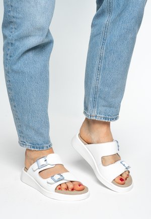 White sandals with two adjustable straps and silver buckles. Cushioned footbed on a thick, white platform sole. Worn with light blue jeans.