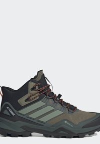 Zapato de senderismo de caña alta en negro y verde oliva con cordones con acentos naranjas, suela texturizada y etiqueta impermeable Gore-Tex.