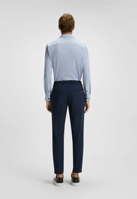 Camicia azzurro chiaro con motivo e colletto strutturato, abbinata a pantaloni blu scuro. Vengono indossate sneakers nere con suola bianca.