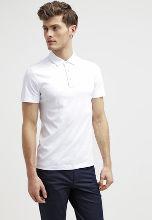 Hvit kortermet polo skjorte med klassisk krage og tre-knapps placket, kombinert med mørk marineblå bukser, glatt stoffstruktur.