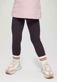 Leggings viola con una texture liscia e un design aderente, abbinati a sneakers chiare con accenti rosa e grigi e calze a righe.