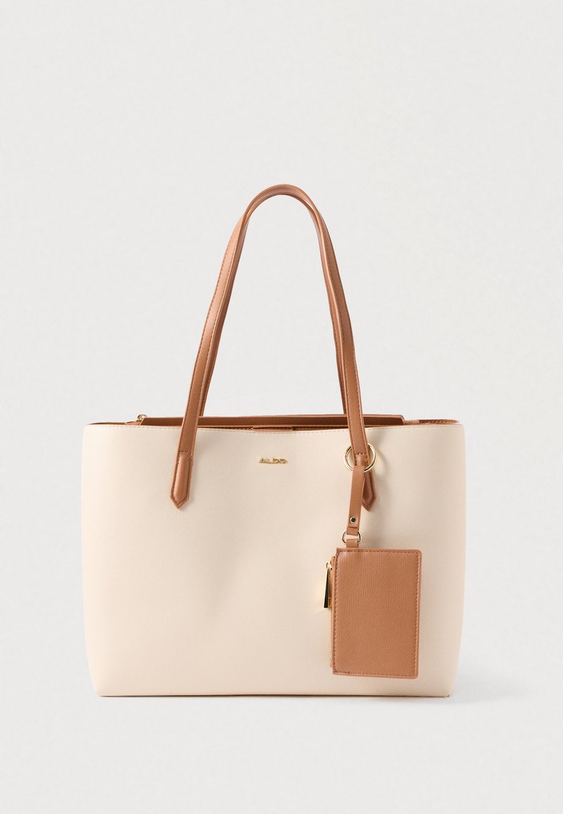 Sac fourre-tout beige avec des accents en cuir marron, texture lisse et deux longues poignées. Comprend un porte-carte détachable. Détail du logo en doré.